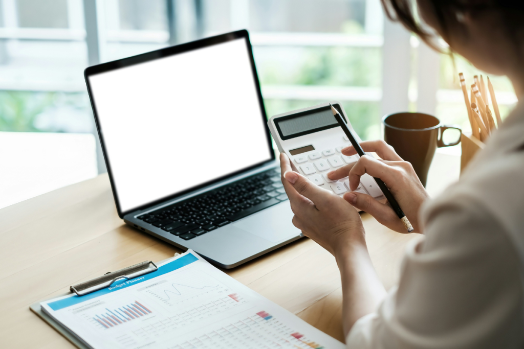 A imagem mostra uma pessoa realizando atividades financeiras ou de planejamento orçamentário em um ambiente de escritório, possivelmente em casa (home office).