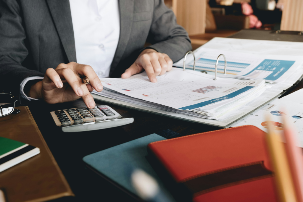 A imagem mostra uma pessoa trabalhando com documentos financeiros, destacando-se um ambiente típico de escritório ou setor administrativo.