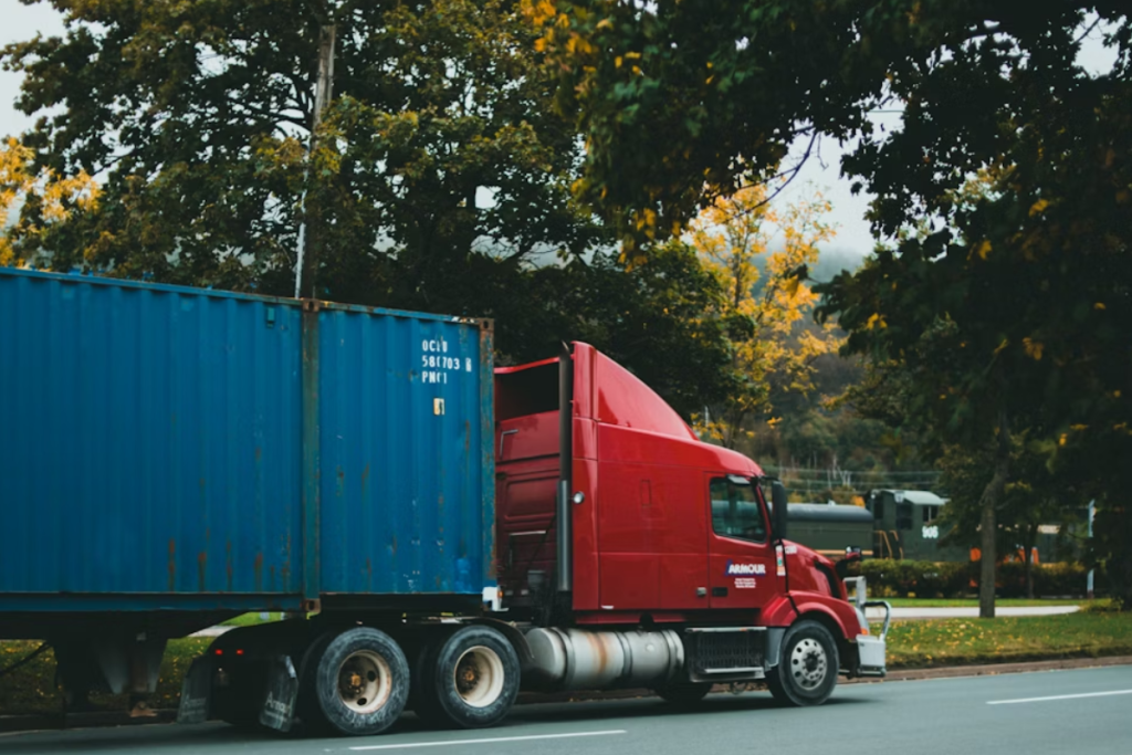 A imagem mostra um caminhão de semi-reboque (ou carreta) parado ou em movimento lento na lateral de uma estrada.
